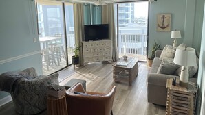 Een ruime woonkamer met een groot raam, een plafondventilator, een flatscreen televisie, een bank, een salontafel en een lamp.