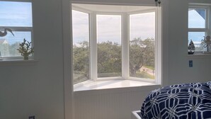 Une pièce dotée d’une baie vitrée, d’un lit recouvert d’une couvre-lit à motifs et d’une petite étagère ornée d’objets décoratifs.