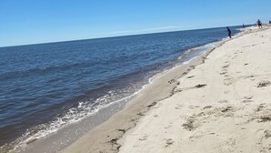 Une plage avec un ciel dégagé, une mer calme et des empreintes de pas dans le sable.