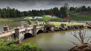 Un puente de piedra sobre un lago tranquilo, con un campo de golf al fondo.