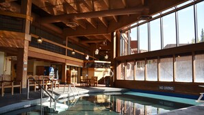 An indoor swimming pool with a 'No Diving' sign, wooden beams, and a view of the outside through large windows.