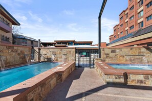Piscina com paredes de pedra e uma cascata, cercada por um edifício com fachada vermelha e várias janelas.