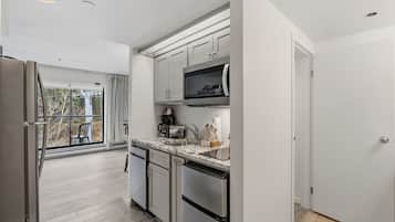 A modern kitchen with stainless steel appliances, a marble countertop, and a view to the outside.