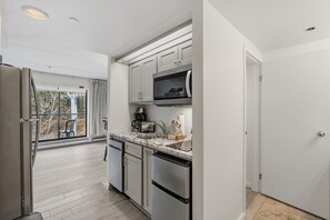 A modern kitchen with stainless steel appliances, a marble countertop, and a view to the outside.