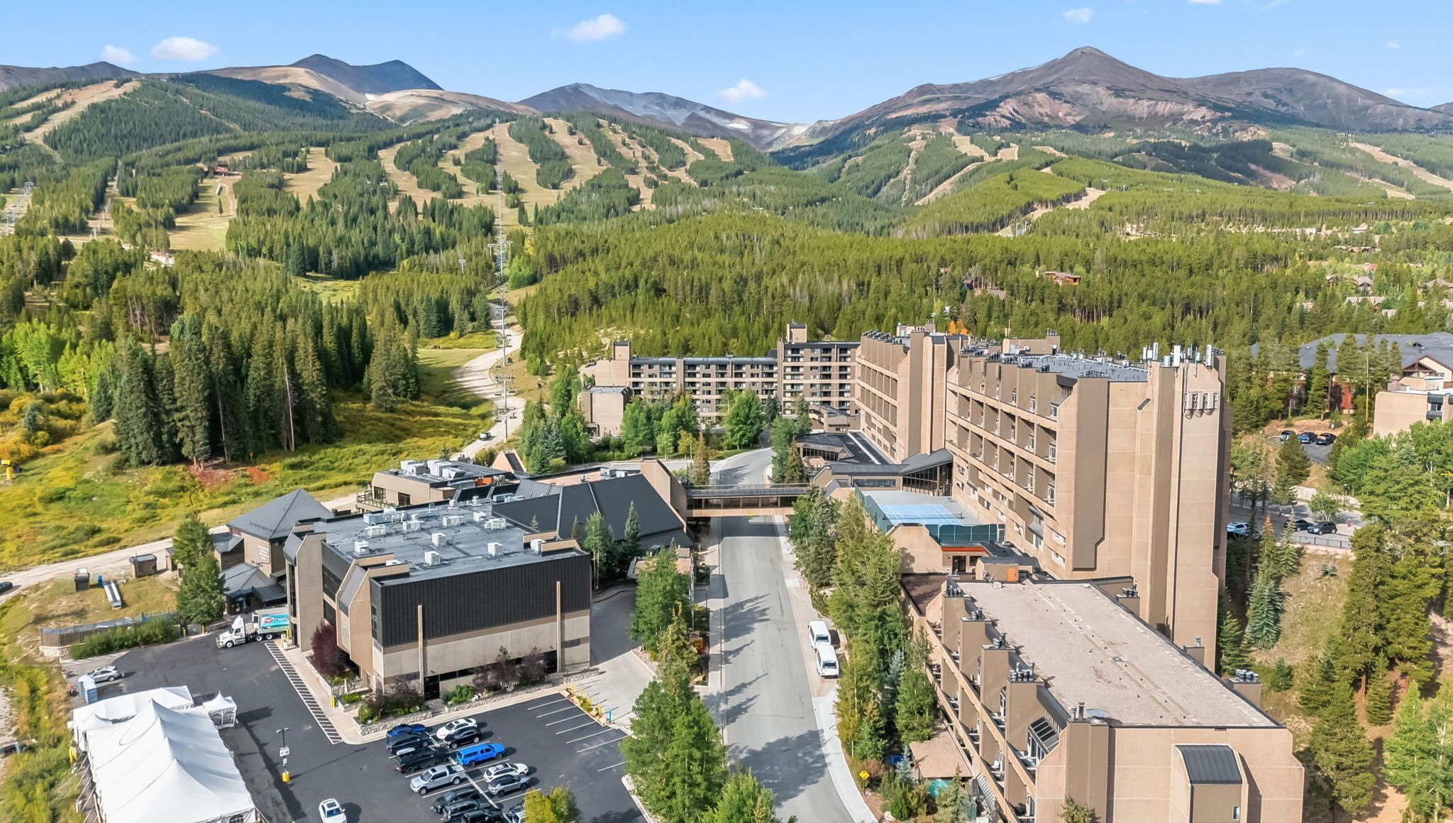 Un complejo hotelero con varias edificaciones, zonas de estacionamiento y montañas al fondo.