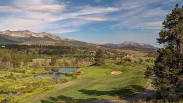A golf course with a pond, surrounded by mountains and trees.
