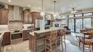 A spacious kitchen with wooden cabinets, stainless steel appliances, and a large island with bar stools. - Stunning Breckenridge Townhome with Private Hot Tub, Garage! (Breckenridge)