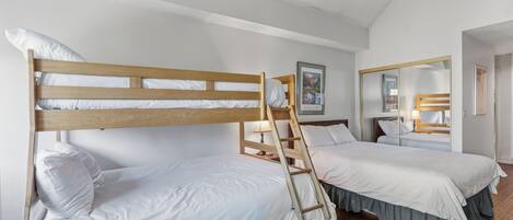 Una stanza con due letti a castello, testiere in legno, biancheria da letto bianca, una scala in legno, un quadro appeso alla parete, uno specchio e un pavimento di legno.
