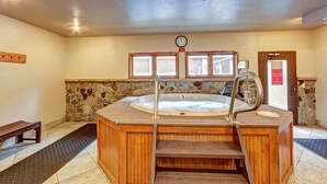 Un bain à remous avec des marches en bois, un mur en pierre, une horloge et une porte ornée d’un panneau d’avertissement.