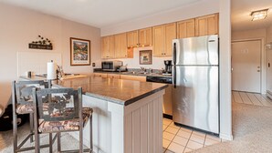 A modern kitchen with wooden cabinets, a stainless steel refrigerator, and a central island with chairs. - Stay Downtown and Quick Walk to Quicksilver Lift! (Breckenridge)