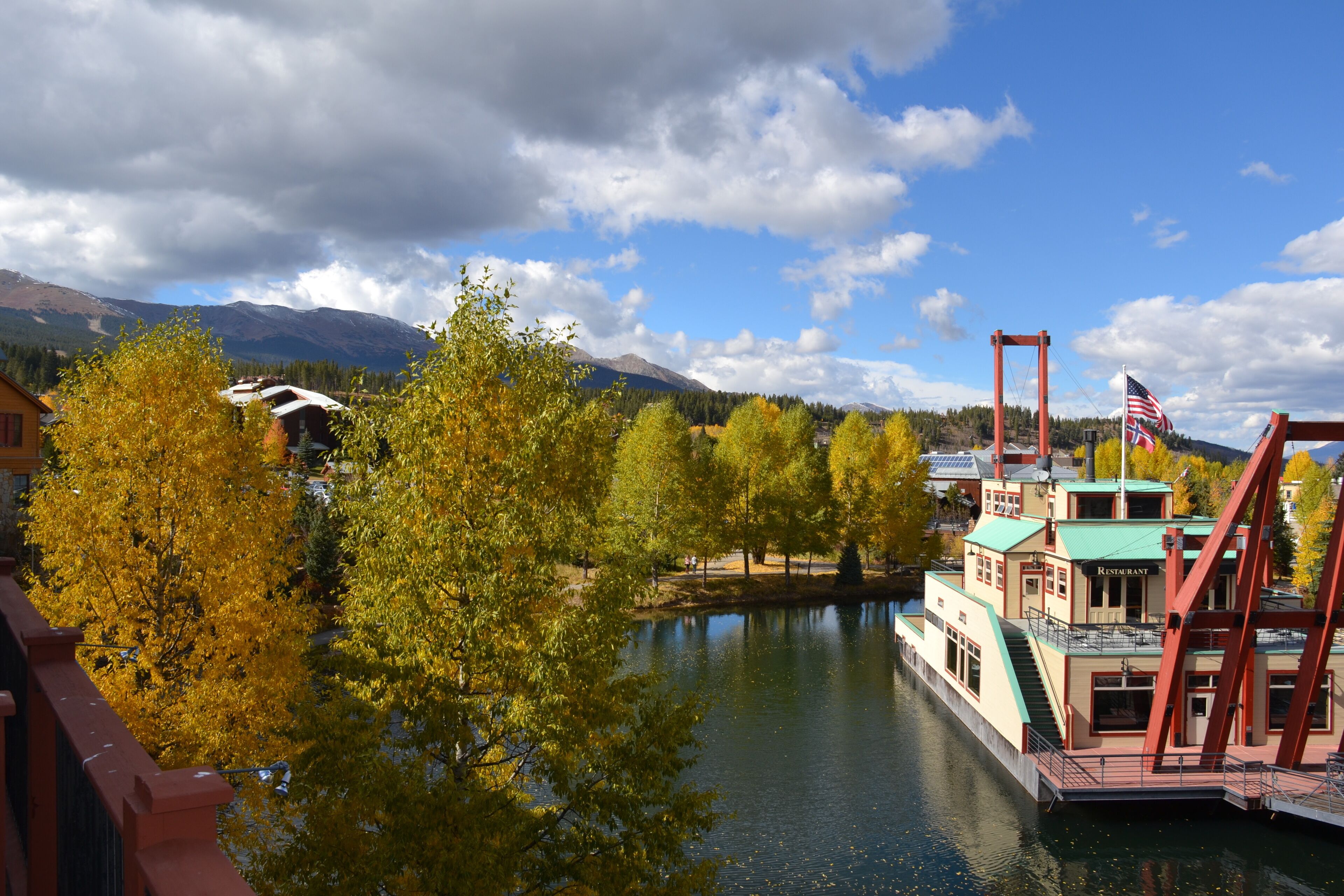 Ein Flussdampfer mit Restaurant auf einem ruhigen Fluss, umgeben von Herbstbäumen und Bergen im Hintergrund.