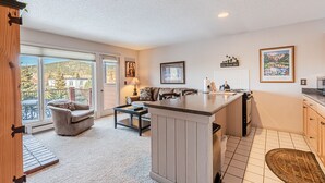A spacious living area with a large window, a sofa, a coffee table, and a kitchen area with a counter and appliances. - Stay Downtown and Quick Walk to Quicksilver Lift! (Breckenridge)