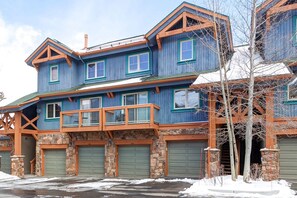 A two-story house with a stone foundation, multiple garage doors, and a wooden balcony. - Breckenridge Townhome Near Lift, Private Garage! (Breckenridge)