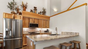 Una cocina con armarios de madera, electrodomésticos de acero inoxidable, encimera de granito y una zona de taburetes de bar.