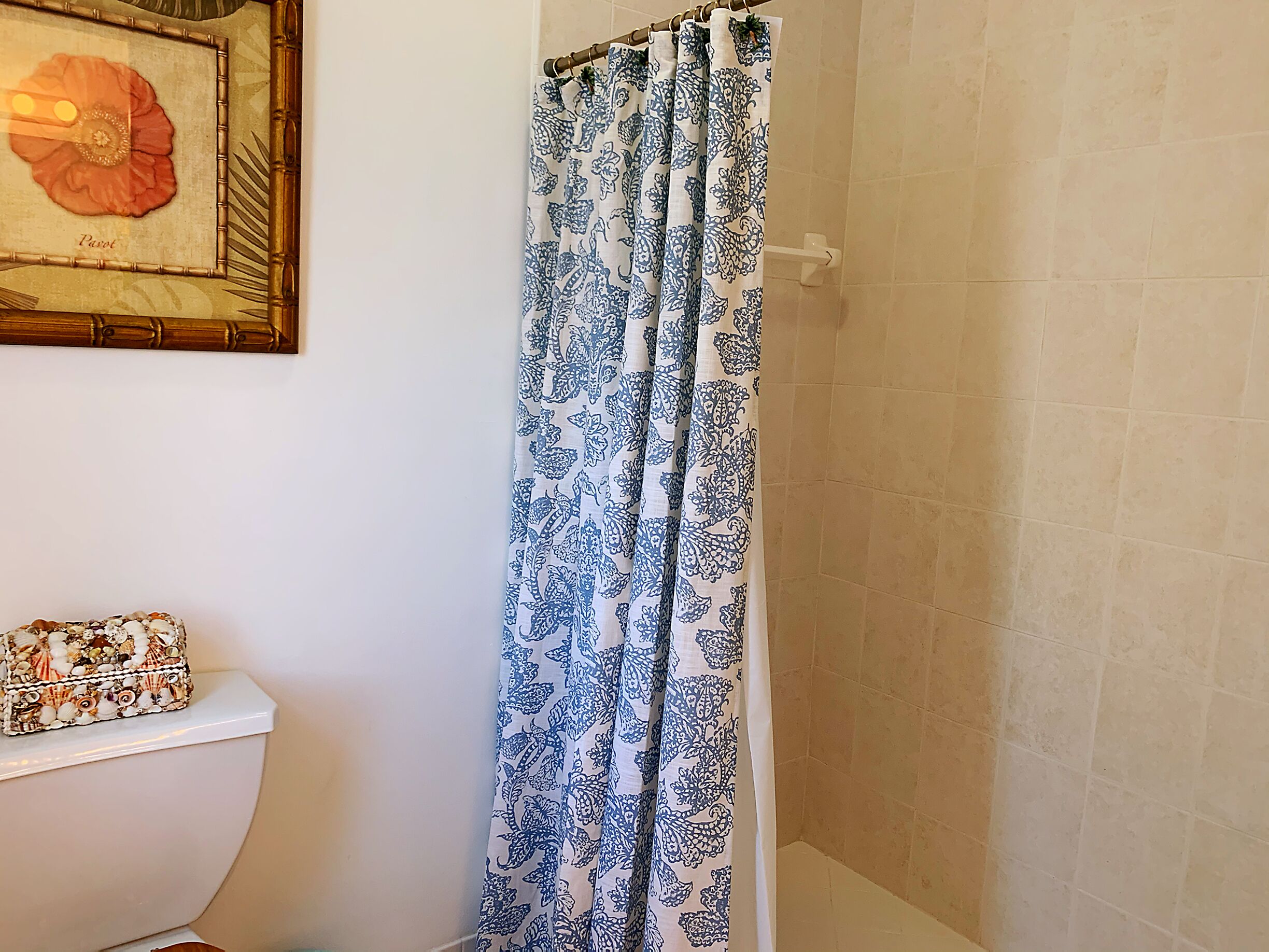 A bathroom with a toilet, a framed artwork on the wall, and a shower curtain with a blue floral pattern.