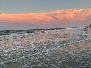 Une plage avec des vagues, un coucher de soleil et quelques personnes.
