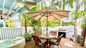 A covered outdoor patio with a round table and wicker chairs, a hot tub, and a white picket fence.