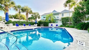 A swimming pool with lounge chairs, palm trees, and a white picket fence in the background.