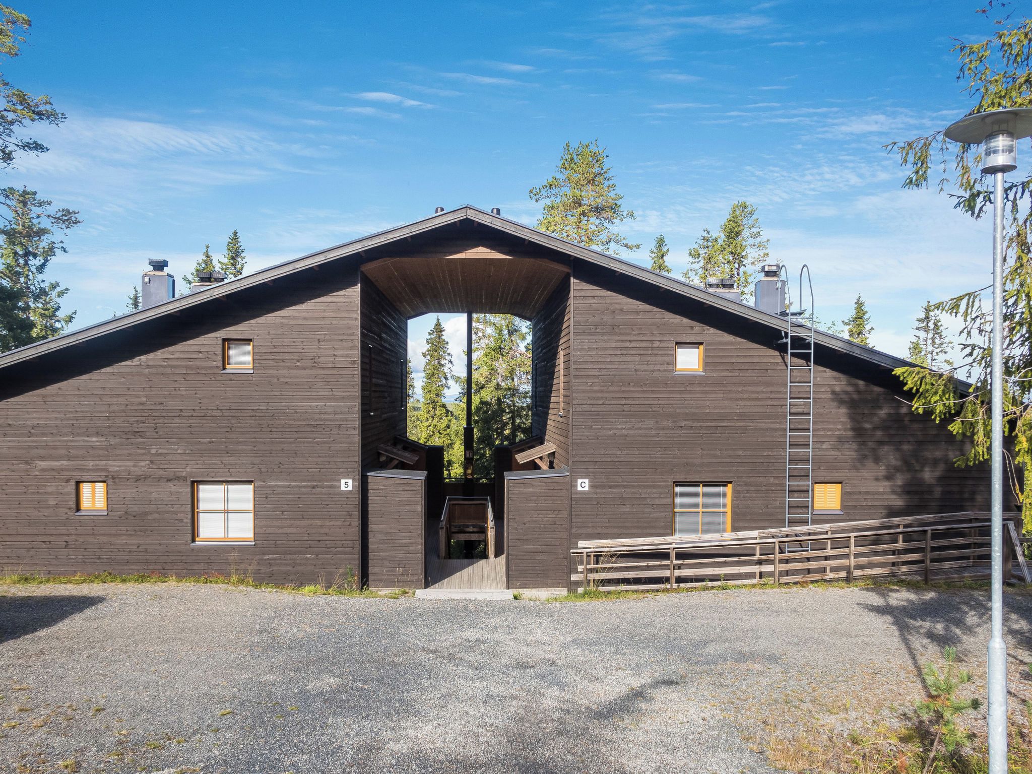 A large wooden building with a central archway, multiple windows, and a gravel driveway.