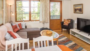 A cozy living room with a sofa, a TV, a dining table, and a window with curtains.