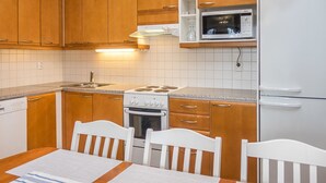 A compact kitchen with wooden cabinets, a white stove, a microwave, and a dining table with chairs.
