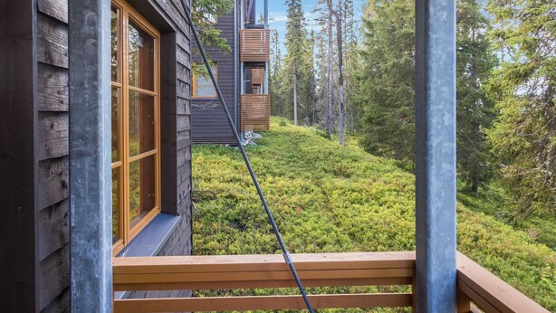 A wooden cabin with a balcony overlooking a forested area.