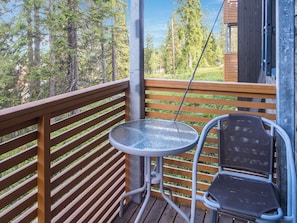 A balcony with a metal table and chairs, overlooking a forested area.