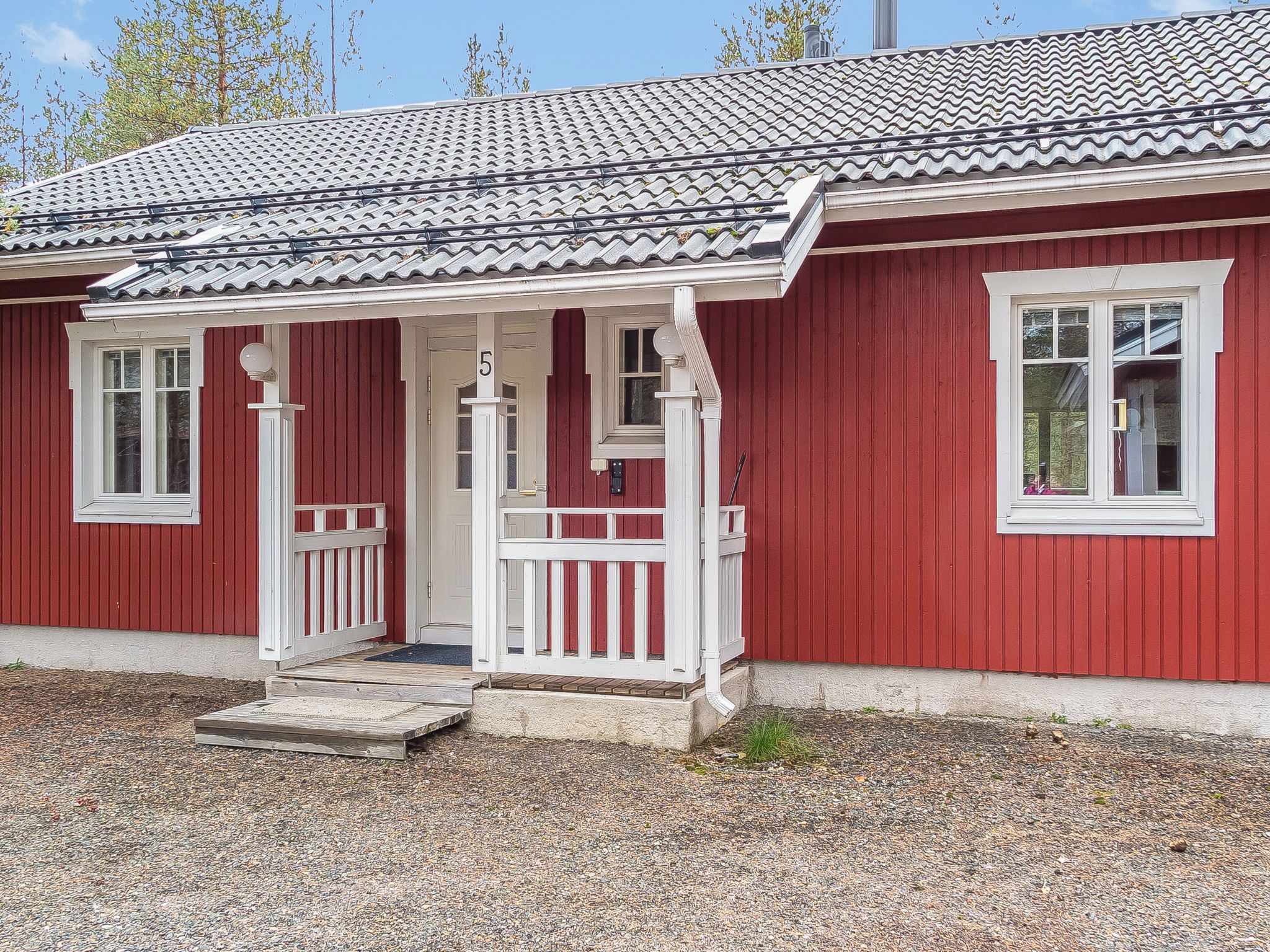Punainen rakennus, jossa on valkoinen kuisti, numeroitu ovi ja ikkuna, josta avautuu näkymä taivaalle.