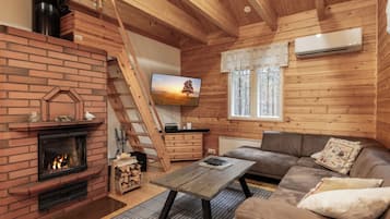 A cozy cabin interior with a fireplace, a wooden ladder, a sofa, and a television.