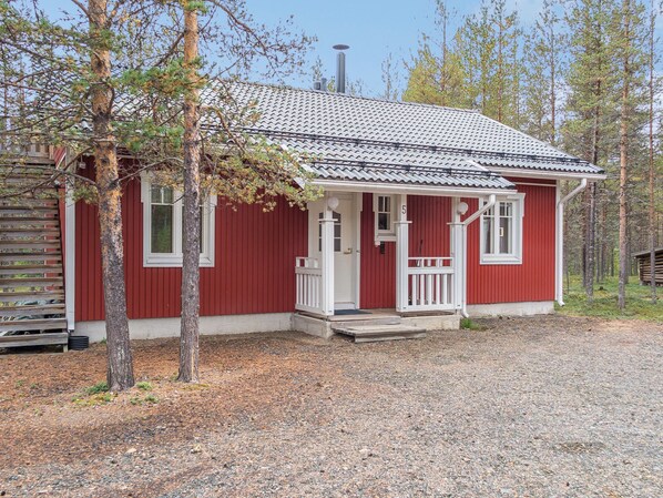 A red wooden cabin with a tiled roof, a porch, and a chimney.