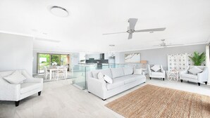A spacious living area with a modern white sofa, a dining table, and a kitchen in the background.