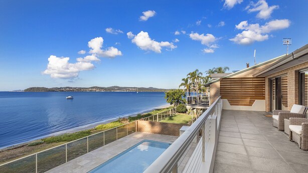A poolside view with a clear blue sky, a body of water, and a distant shoreline.
