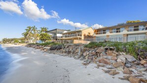 A beachfront property with a sandy beach, a rocky shoreline, and modern buildings with balconies overlooking the sea.