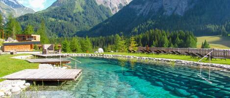 A mountain resort with a clear pool, wooden deck, and lounge chairs.