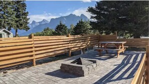 A wooden fence, picnic table, and fire pit in a park with a mountain view.