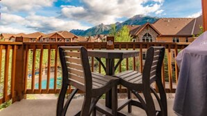 Une terrasse avec deux chaises en bois et une table, d’où l’on peut admirer une chaîne de montagnes et une piscine.