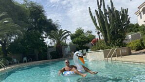 Un home flota sobre un inflable amb forma de cigne a una piscina cristal·lina envoltada de palmeres i cactus.