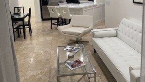 Un saló modern amb una taula de centre de vidre, un sofà blanc i una zona de menjador amb cadires.