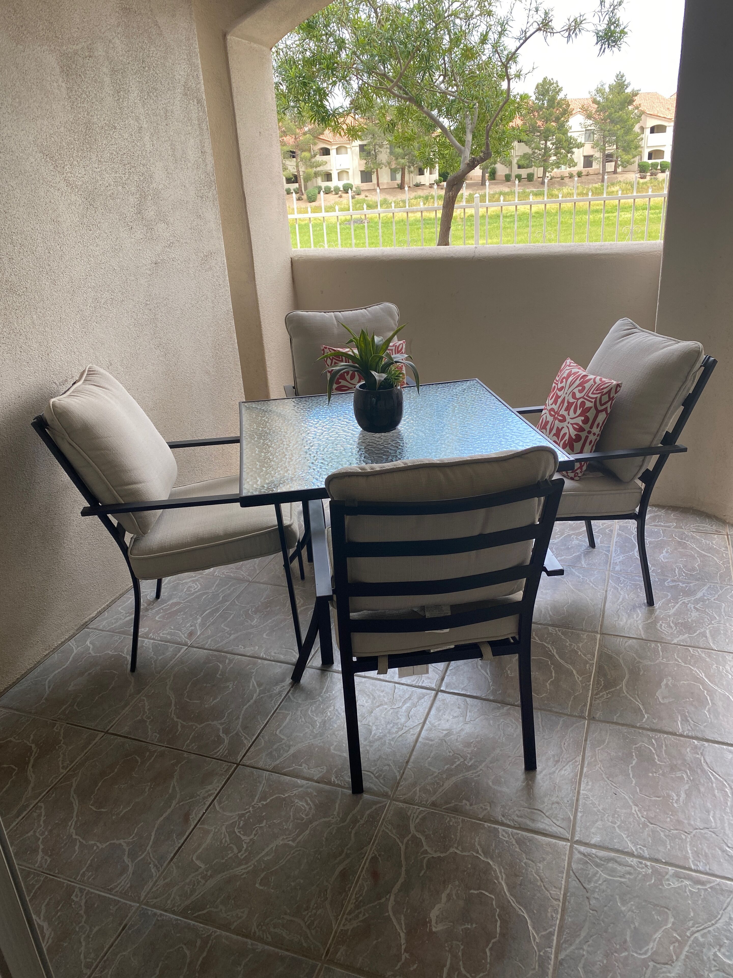 A covered patio with a glass table, four chairs, and a potted plant.