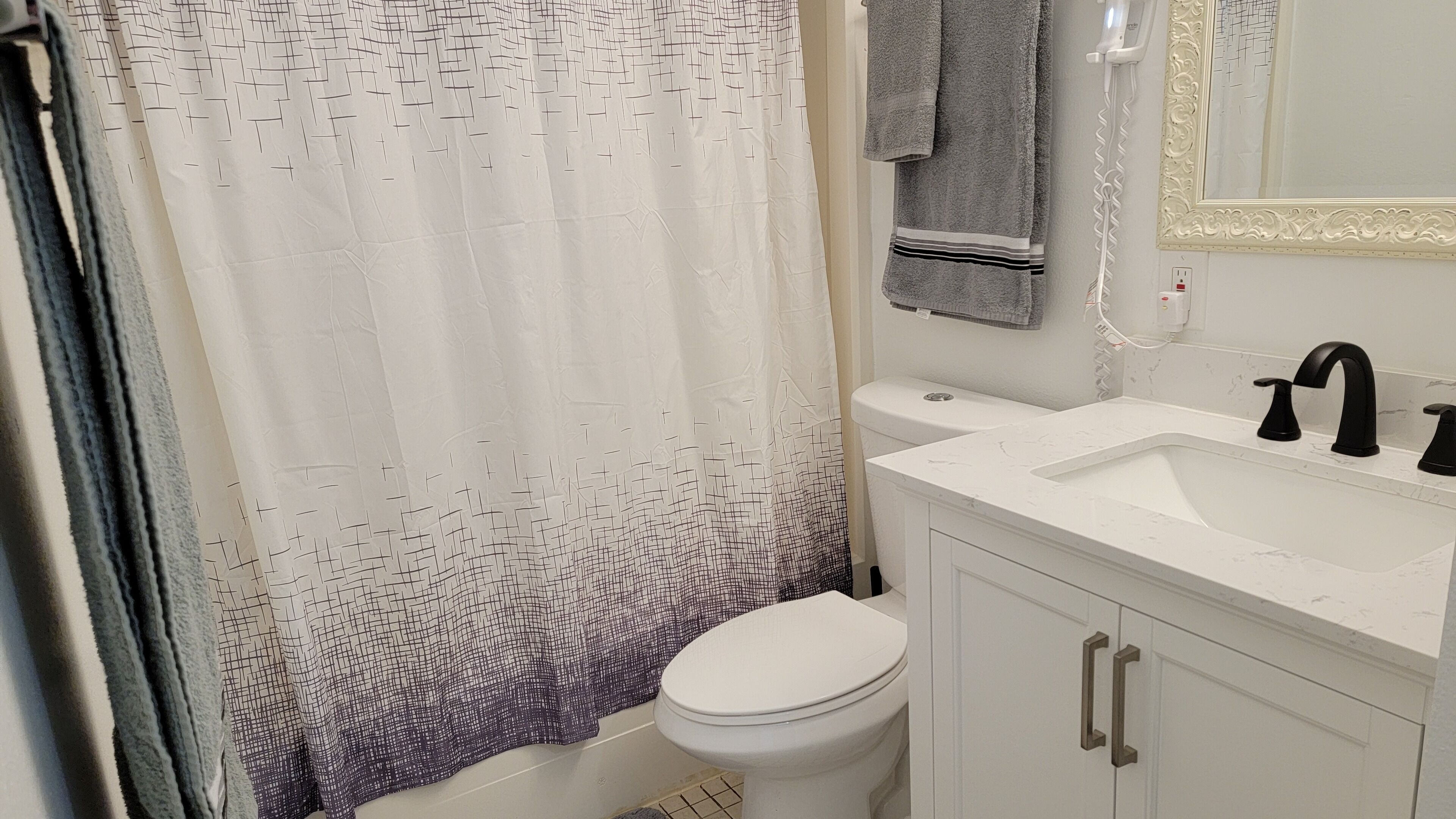A bathroom with a white toilet, a white sink with black faucets, and a shower curtain with a geometric pattern.