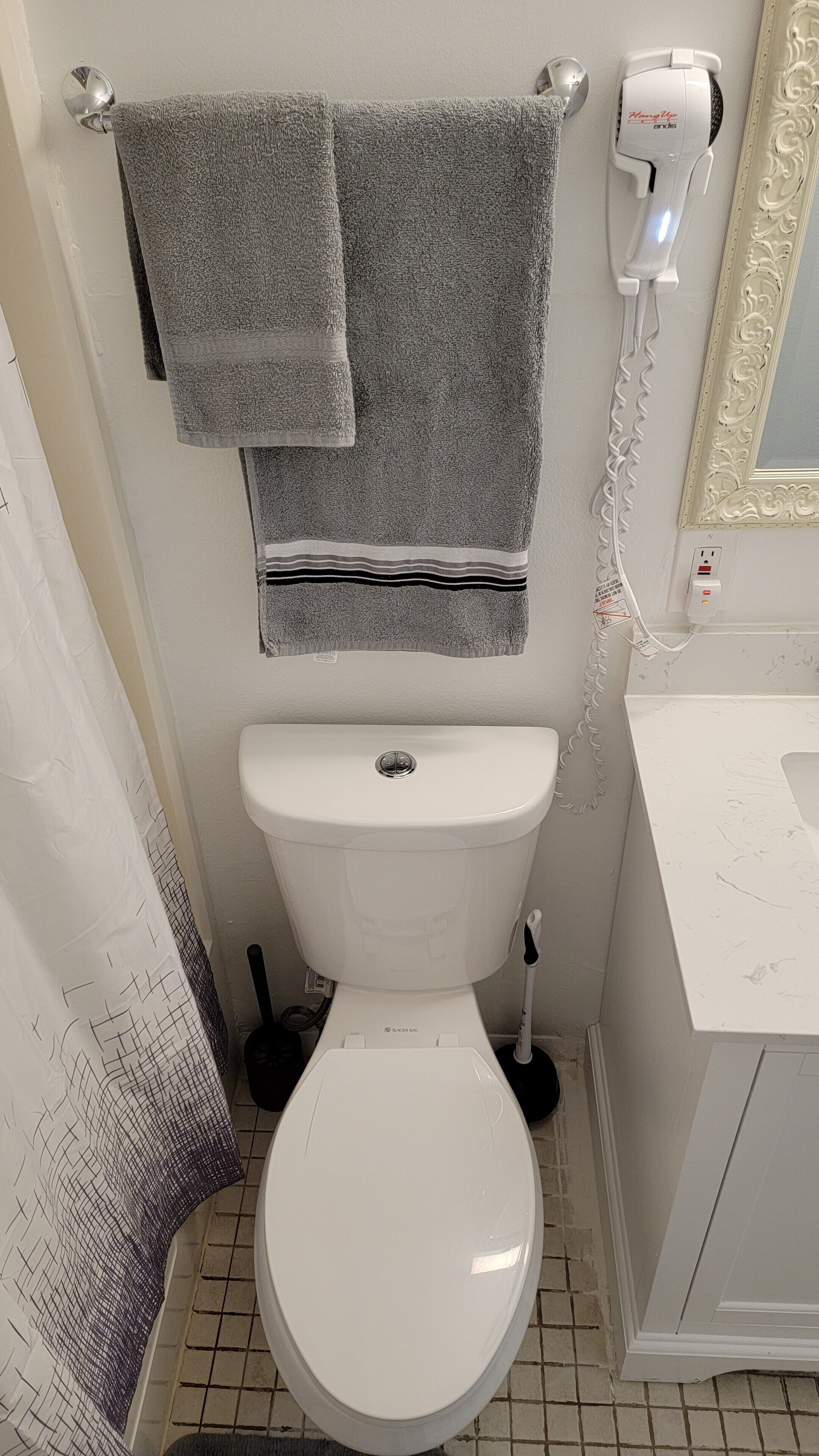 Een badkamer met een wit toilet, een haardroger aan de muur en een handdoek aan een rek.