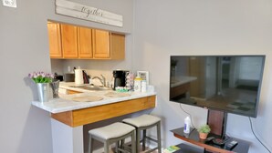 A compact kitchen with a built-in island, wooden cabinets, and a flat-screen TV mounted on the wall. - 🏡Comfy & Convenient 1BR Apartment Near Oaks Mall & Medical Center Fast WIFI (Gainesville)