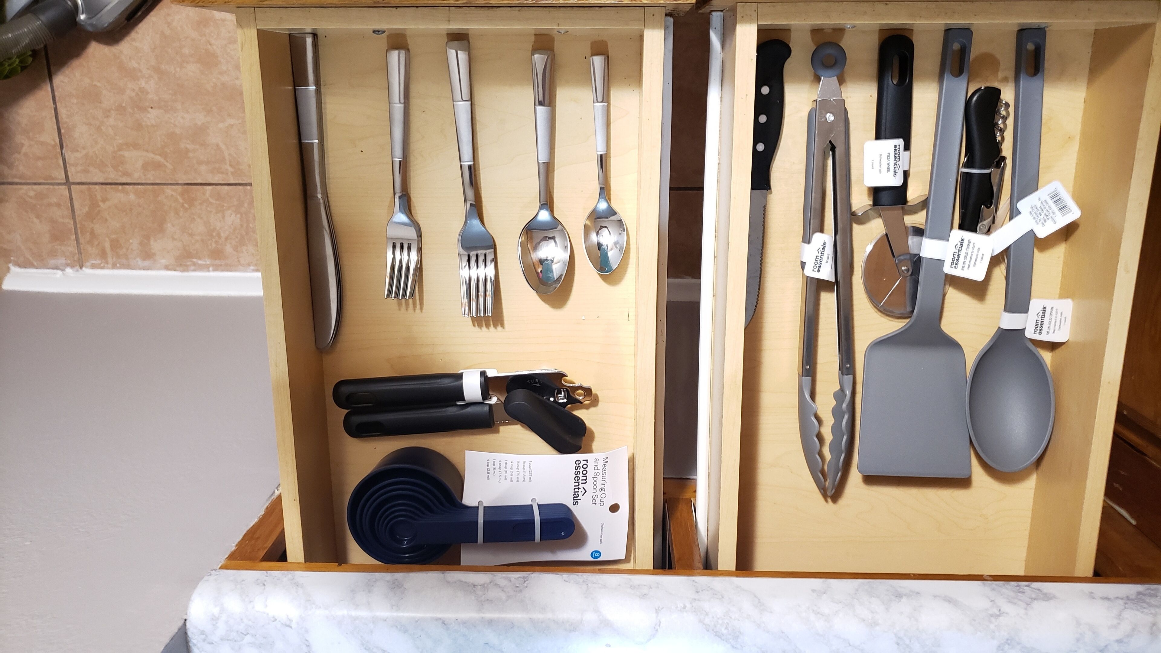 En skuffe med forskellige køkkenredskaber, herunder skeer, gafler, knive og et målebæger.