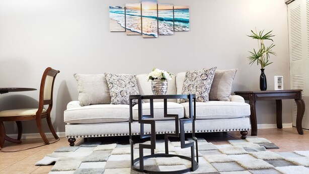 A living room with a sofa, a coffee table, a chair, a rug, and a wall art piece. - 🏡Comfy & Convenient 1BR Apartment Near Oaks Mall & Medical Center Fast WIFI (Gainesville)