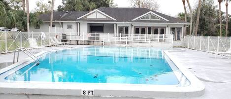 A rectangular swimming pool with a 8 ft. depth marker, surrounded by a white fence, with a house in the background.