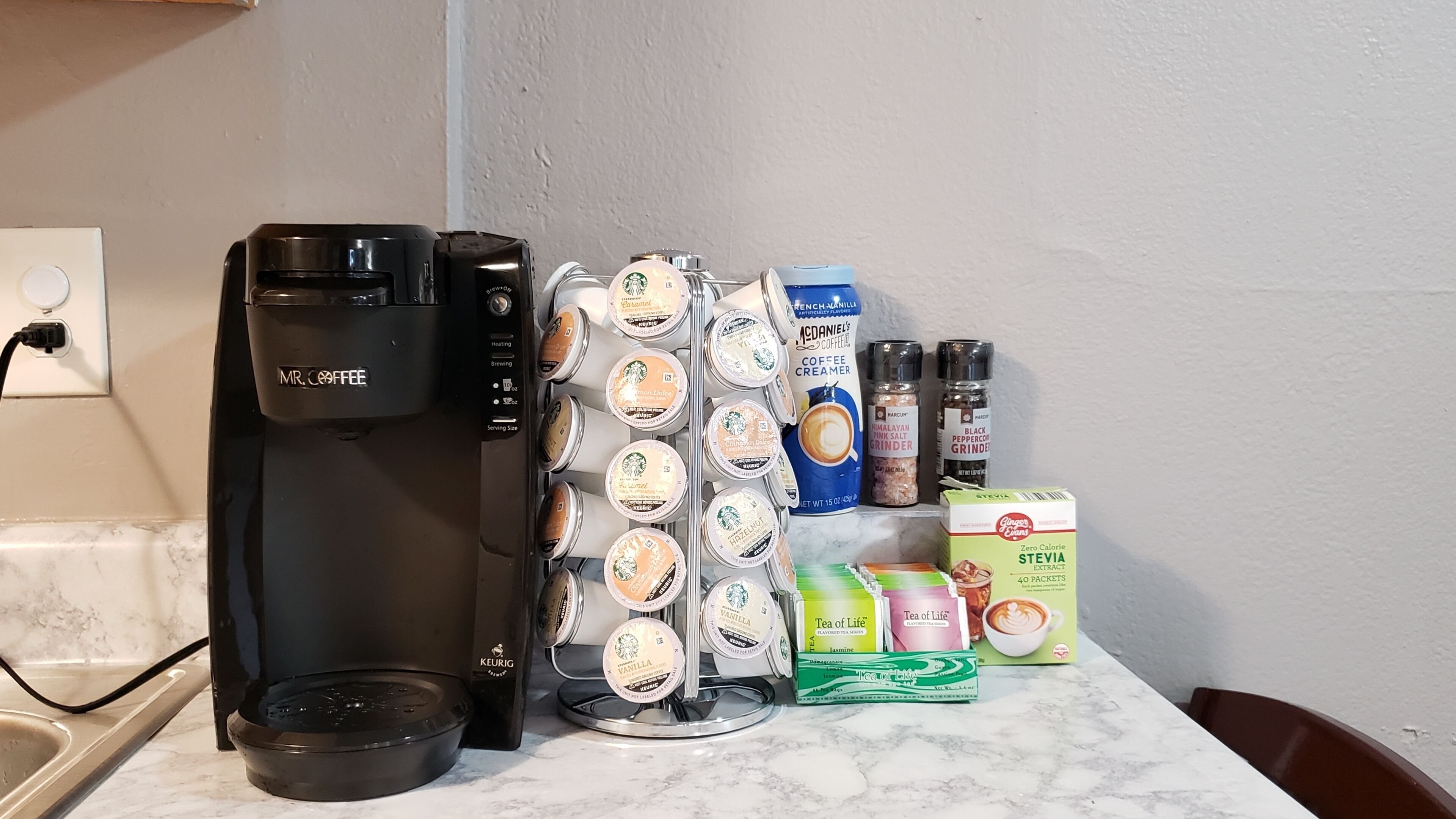 Une machine à café, un moulin à café et divers dosettes de café et sachets de thé sont posés sur un plan de travail de cuisine.