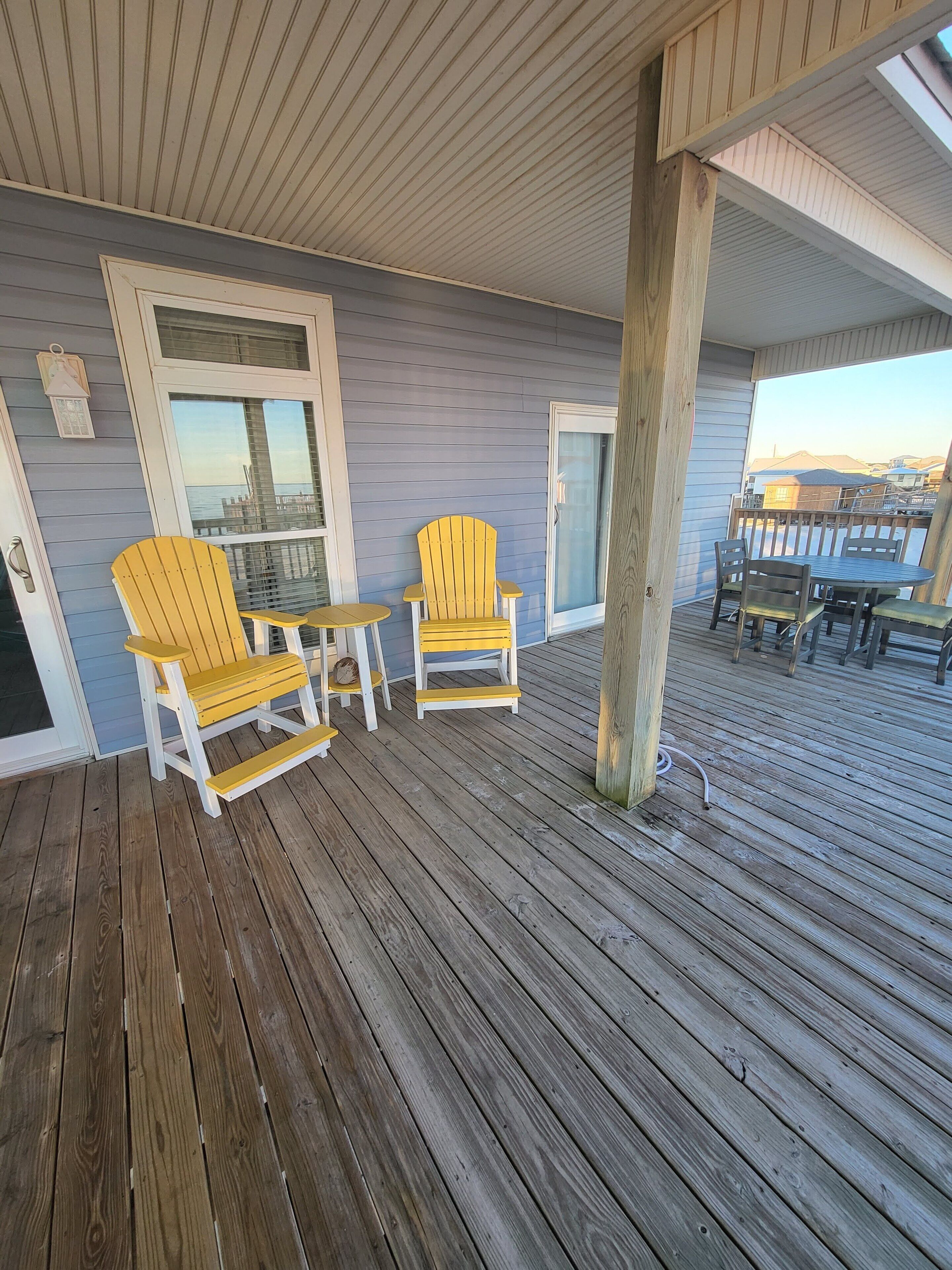 Een houten terras met twee gele Adirondack-stoelen en een bijzettafeltje.