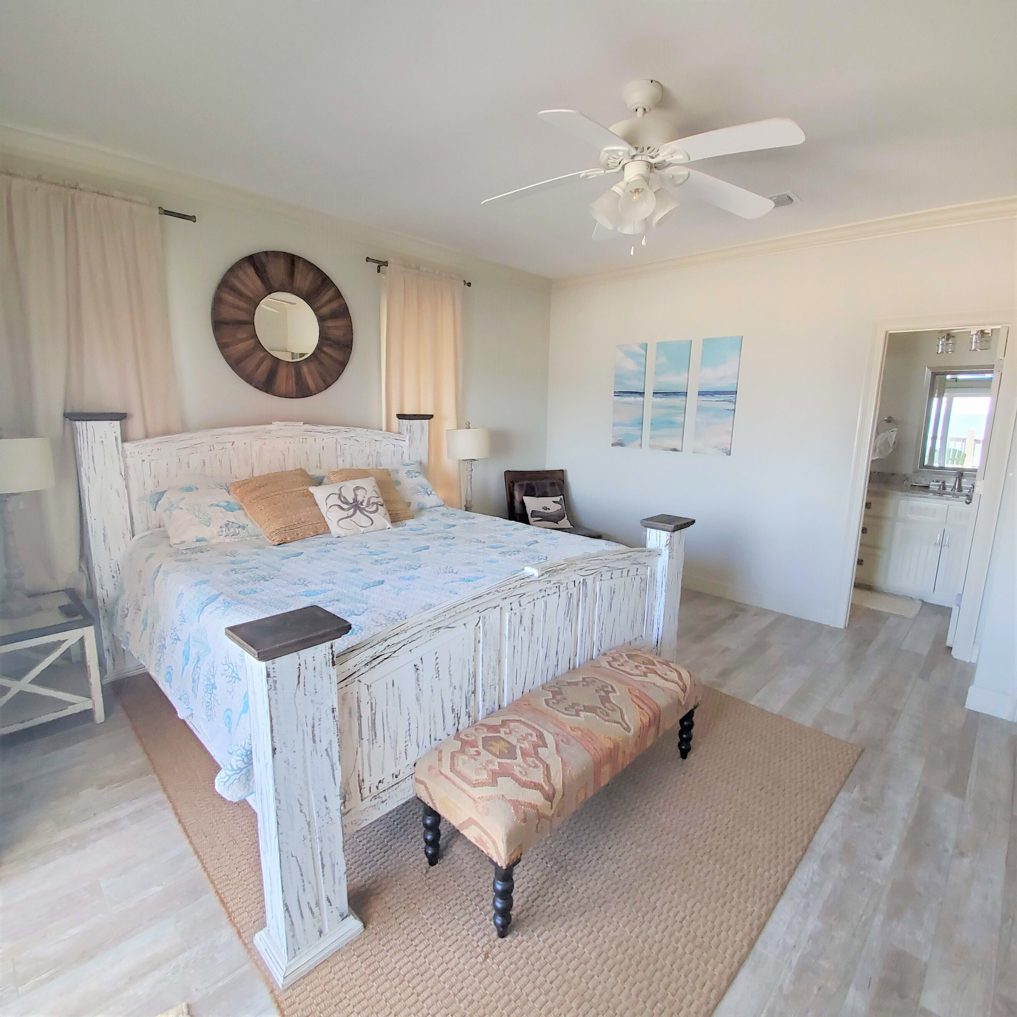 A bedroom with a bed, bedside tables, a ceiling fan, a bench, and artwork on the wall.