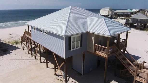 A beach house with a metal roof, wooden deck, and a balcony.