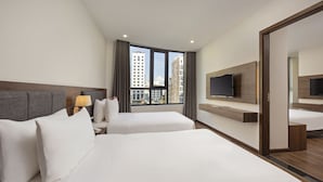 Una habitación de hotel con dos camas, televisión, escritorio y ventana con vista a la ciudad.